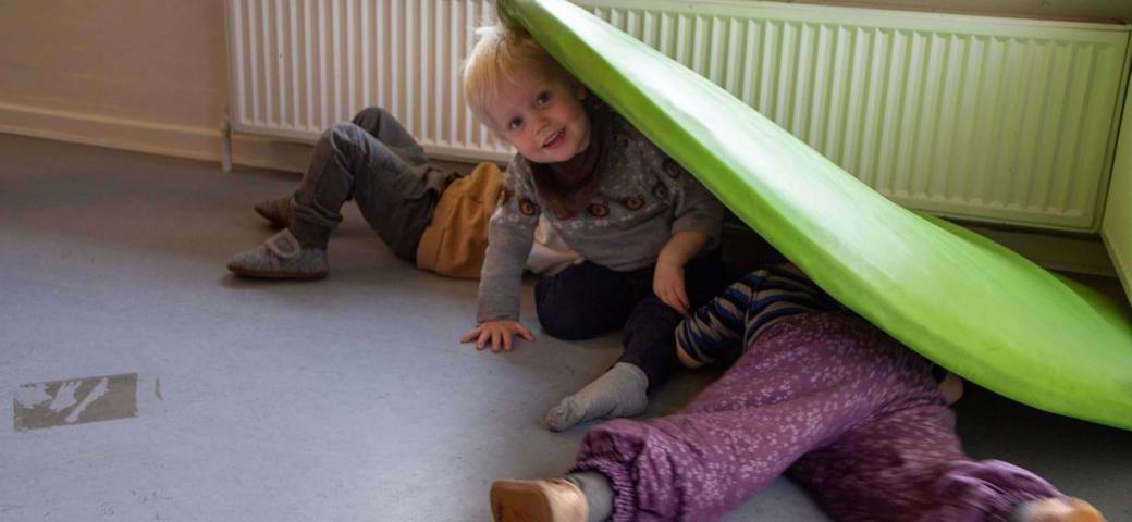 tre børn gemmer sig under en hynde